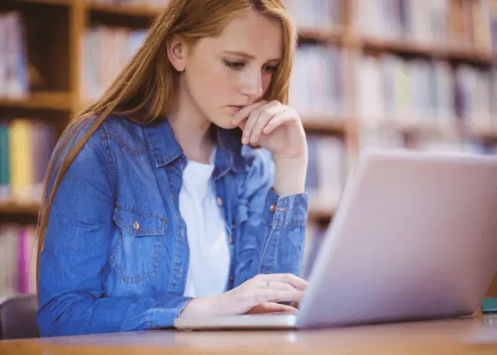 estudiante chica pelirroja en la biblioteca concentrada estudiando en su portátil 