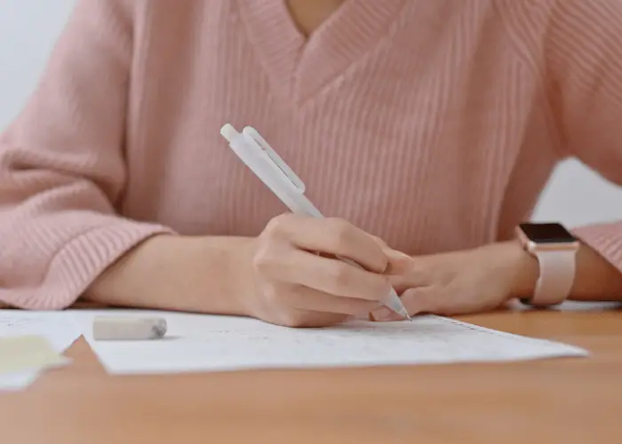 joven vestida de rosa escribiendo un trabajo, estudiando y siendo productiva
