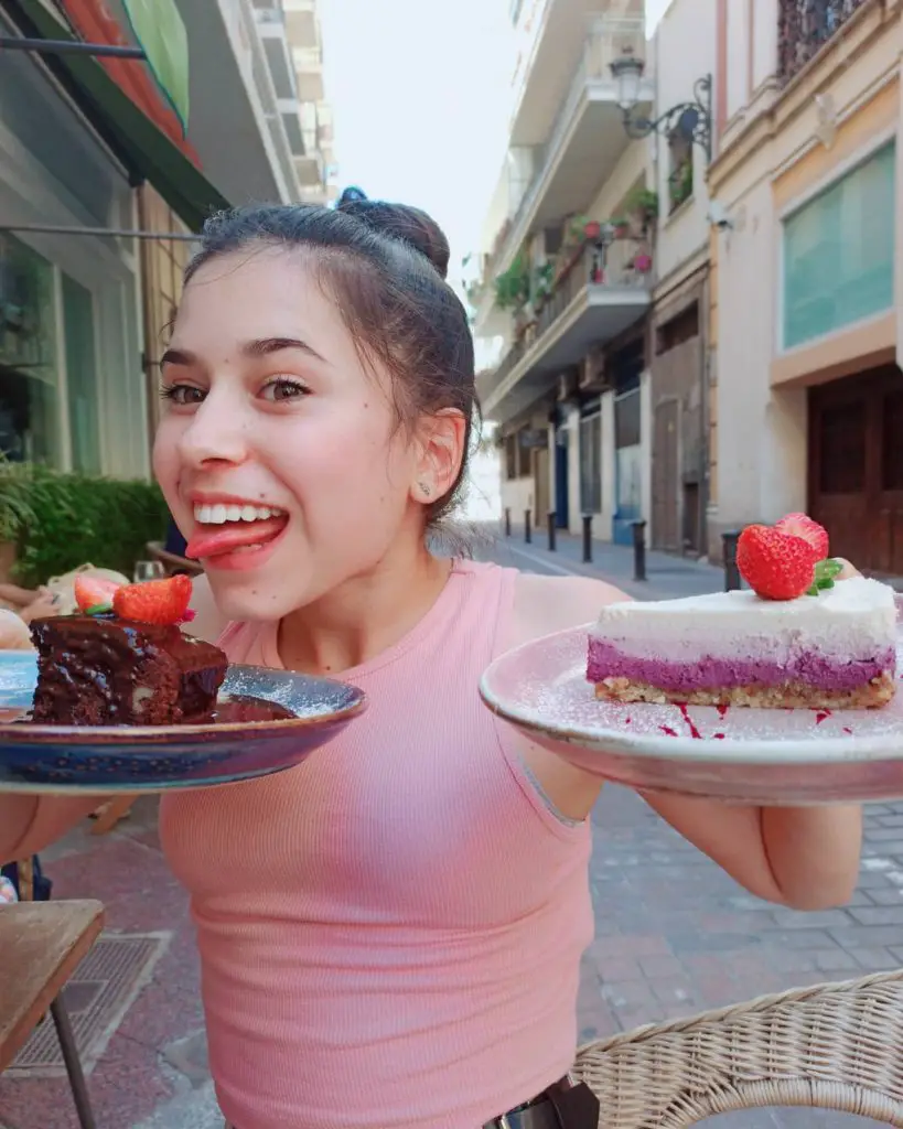 comer de forma intuitiva, comer consciente, intuitive eating, joven vestida con top rosa comiendo postres brownie de chocolate y cheesecake vegano